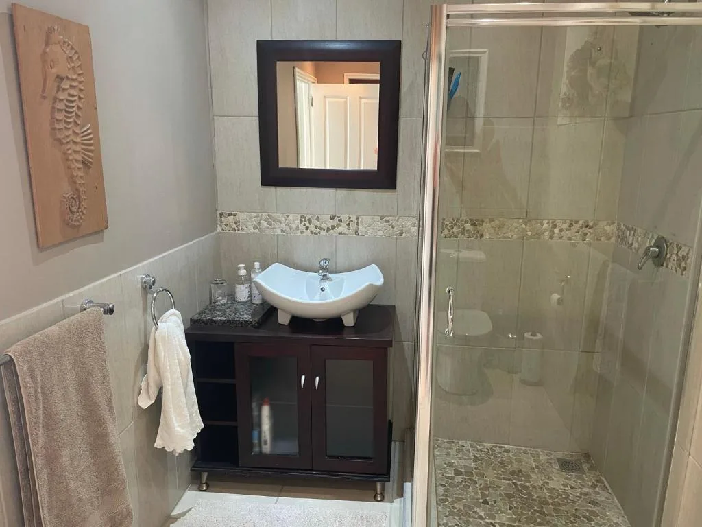 Modern bathroom with white curved sink, dark vanity, and glass shower enclosure