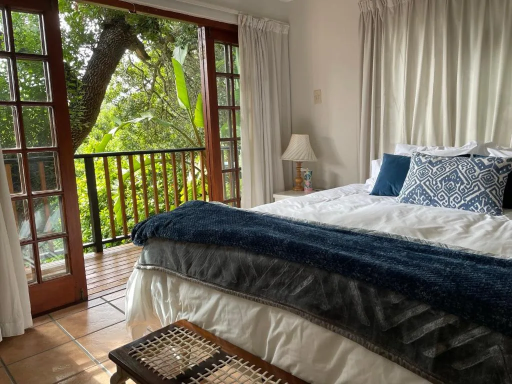 Bright bedroom with bed, open doors to balcony overlooking green trees