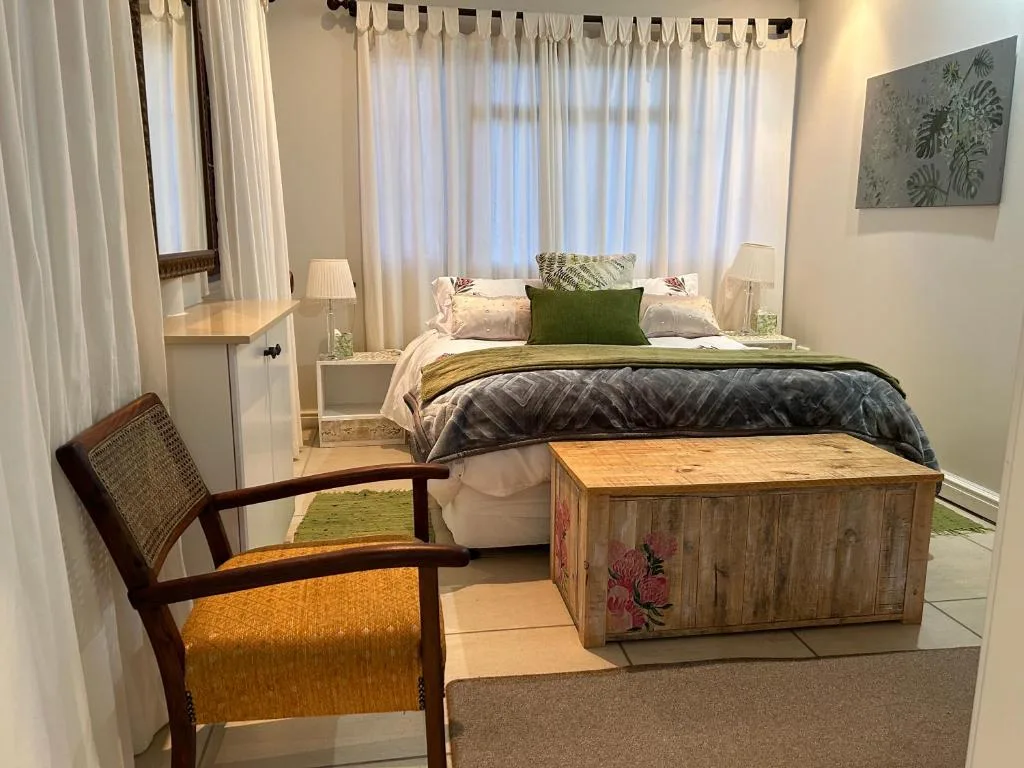 Bright bedroom with queen bed, green cushions, wooden storage chest, and chair