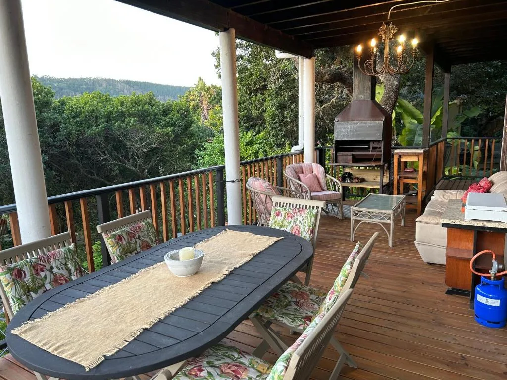 Expansive covered deck with dining table, lounge seating, braai area, overlooking forested valley