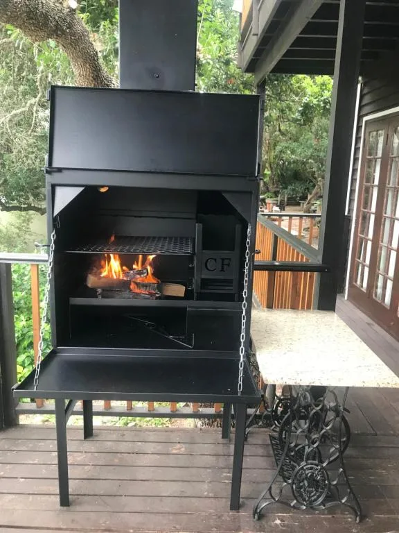 Black outdoor braai grill with active fire on covered wooden deck