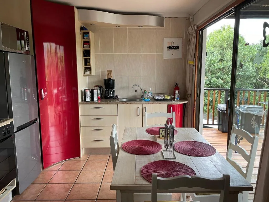 Modern kitchen with red accents, dining table, and garden views through sliding doors