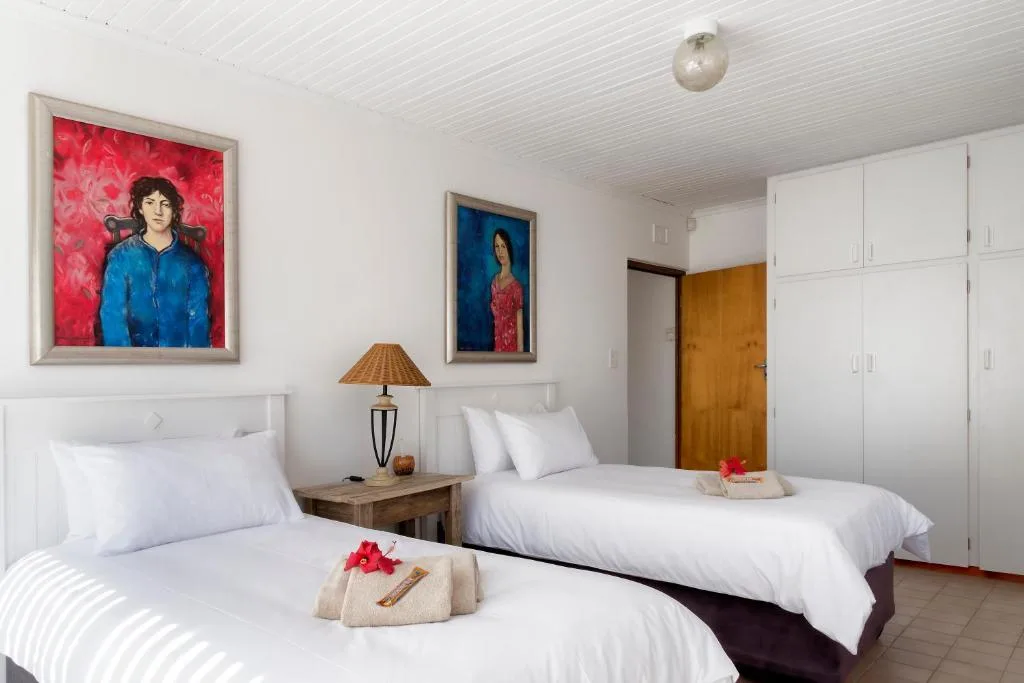 Twin bedroom with white linens, colorful artwork, and wooden storage.