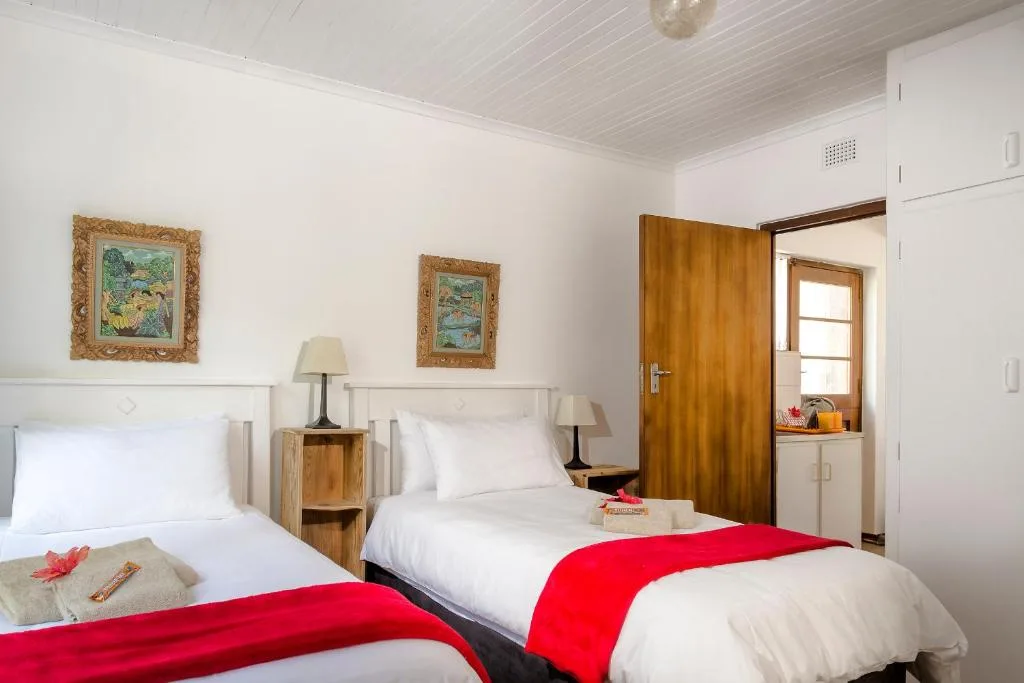 Bright bedroom with two twin beds, red accents, wooden bedside tables, framed artwork
