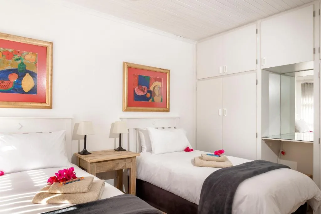 Bright twin bedroom with white bedding, wooden nightstand, colorful wall art