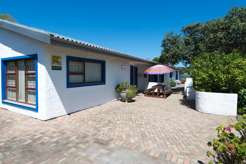 White cottage with blue trim and paved courtyard entrance on sunny day