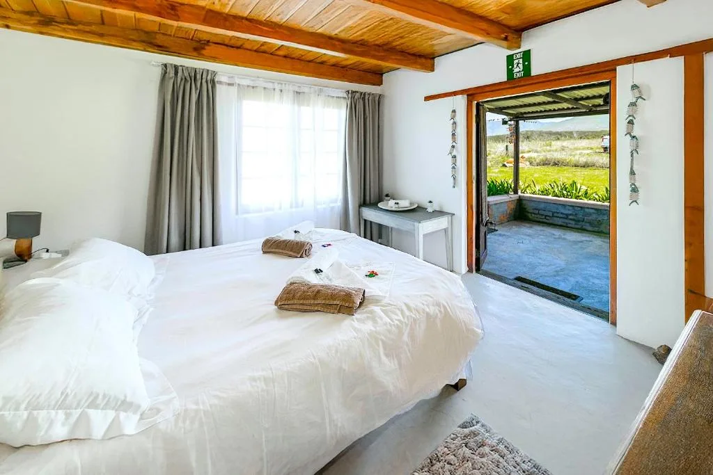 Bright bedroom with queen bed, wooden beams, and garden view through open door