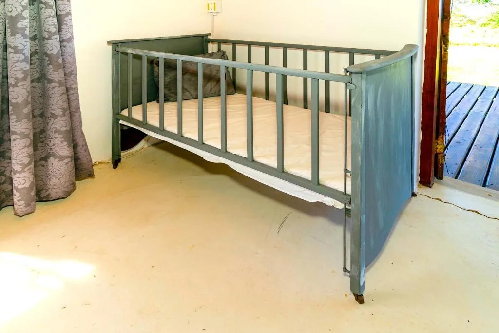 Green wooden crib with white mattress in bright bedroom space