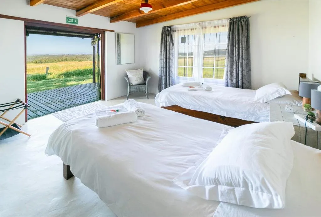 Bright bedroom with two beds, wooden beams, and pastoral views through open doors