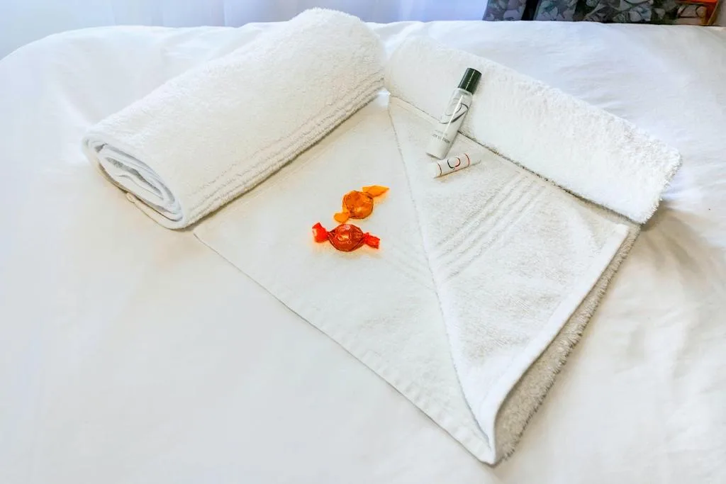Fluffy white towels with welcome sweets and toiletries on bed
