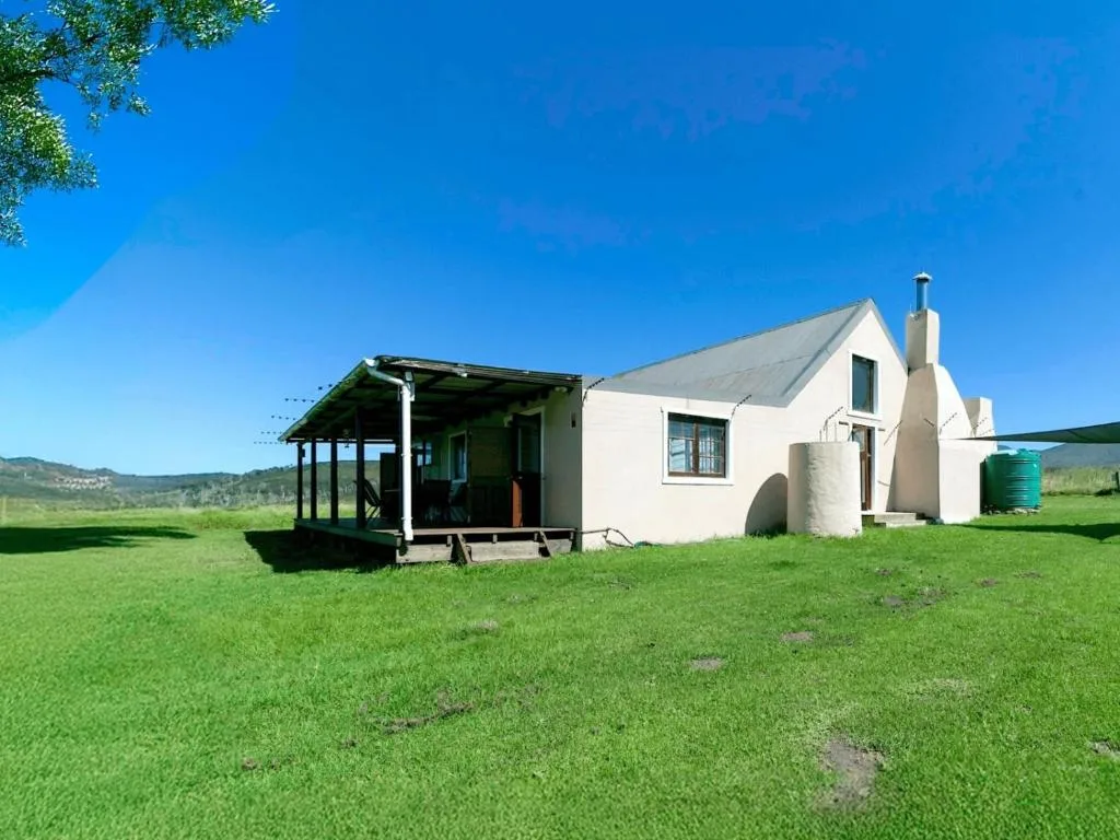 White cottage with covered porch set in green countryside landscape
