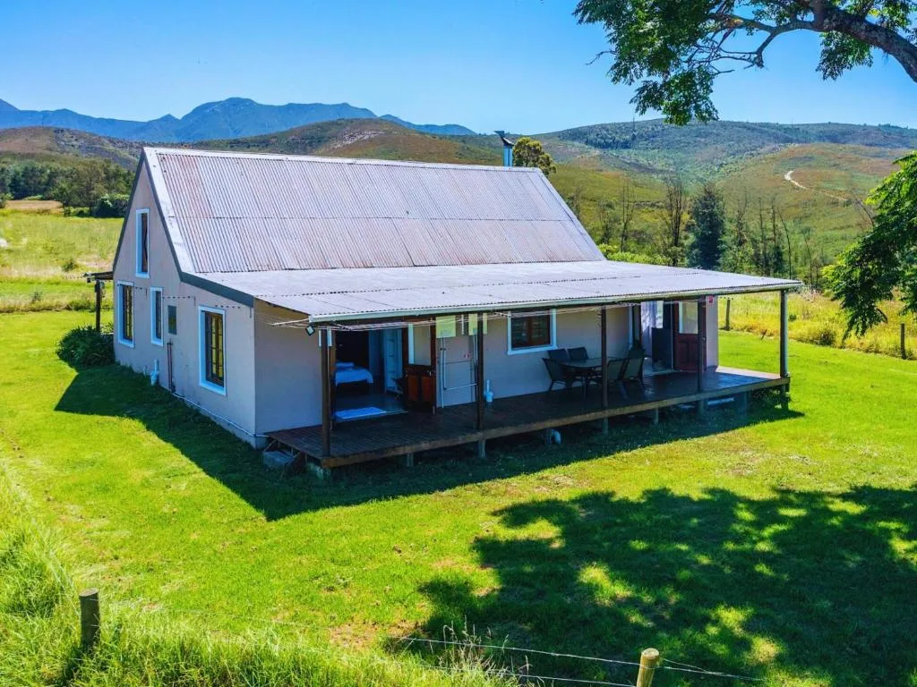 Blue and white cottage with wraparound deck overlooking green valley and mountains