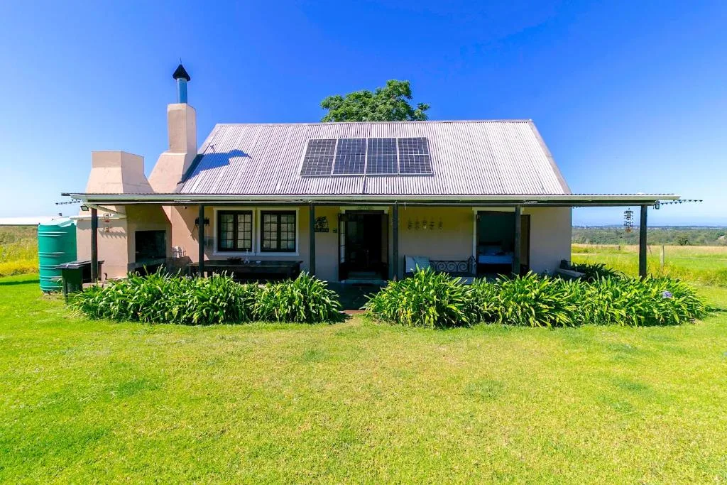 Charming countryside cottage with solar panels and wide veranda, surrounded by green lawn