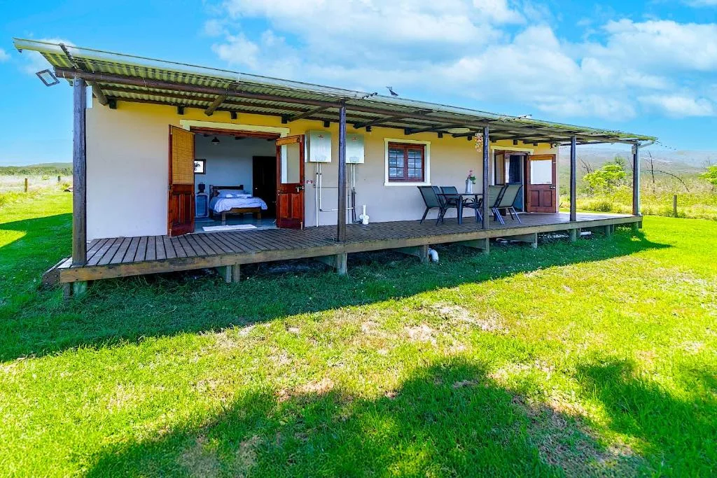 Modern farmhouse with wrap-around deck on green grounds under blue sky