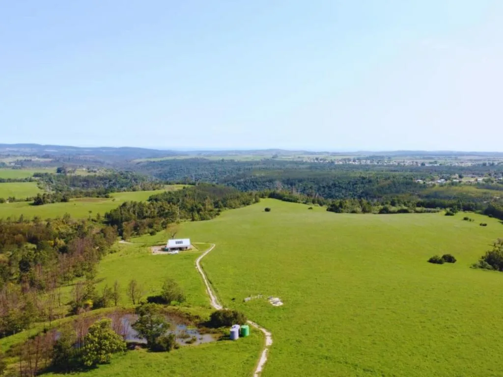 Aerial view of rolling green hills and forests with rural property nestled in valley