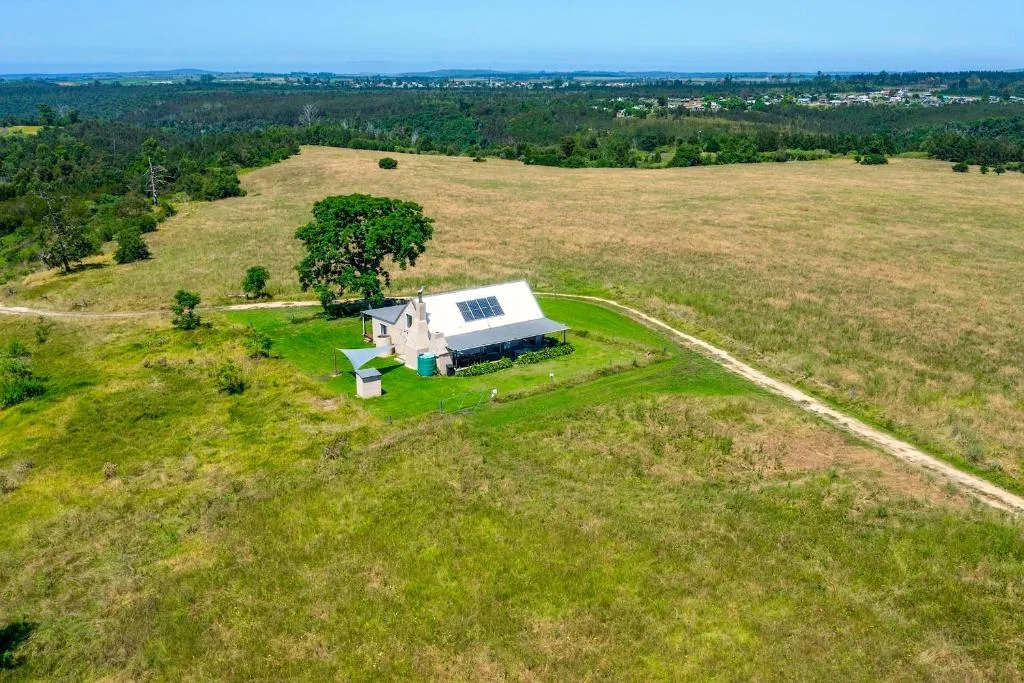 Aerial view of rural property surrounded by green fields and distant forest landscape