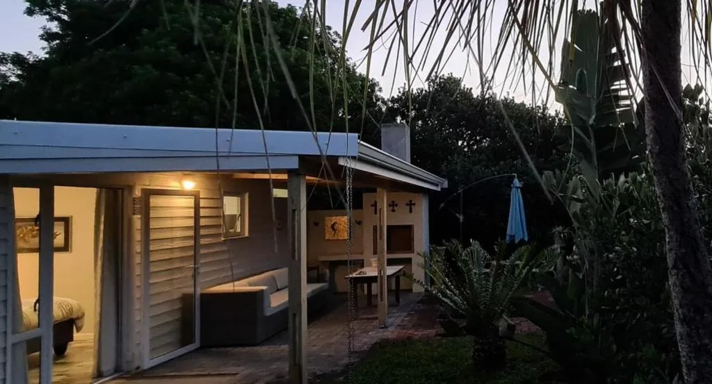 Modern cottage exterior at dusk with illuminated windows and tropical garden setting
