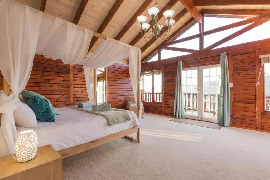 Spacious wooden bedroom with four-poster canopy bed and panoramic windows