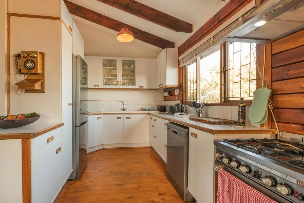 Rustic kitchen with white cabinetry, wooden beams, and stove appliances