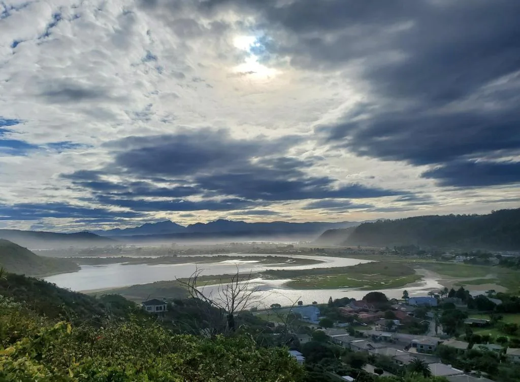 Panoramic valley landscape with lagoon, mountains, and scattered houses below