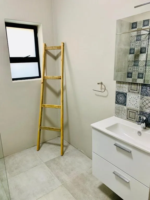 Modern bathroom with white vanity, patterned tile feature wall, and wooden towel ladder