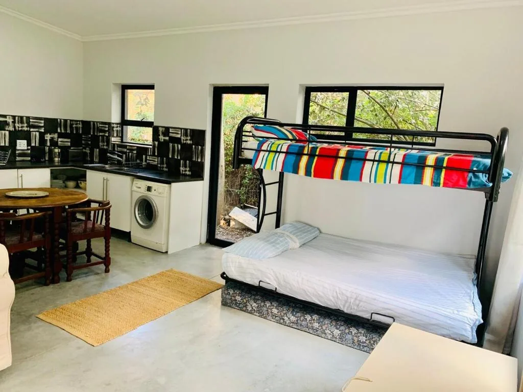 Spacious bedroom with bunk bed, kitchenette, and large windows overlooking garden