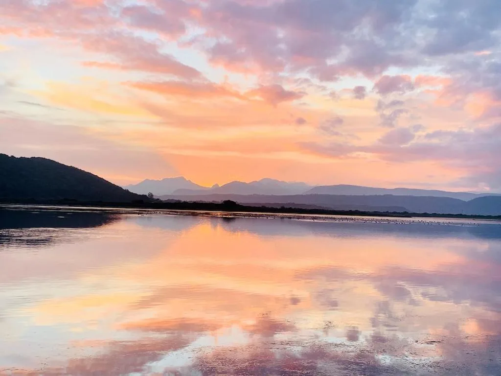 Sunset over lagoon with mountains and dramatic pink sky reflecting on water