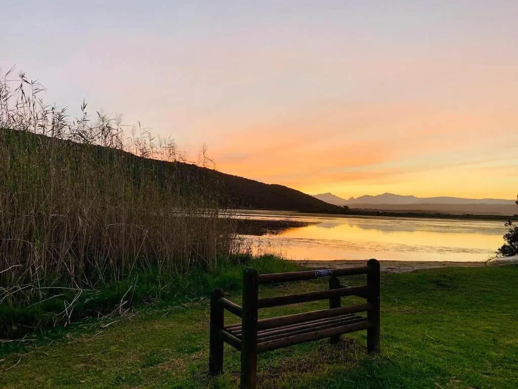 Sunset over lagoon with mountains, bench on grassy foreground