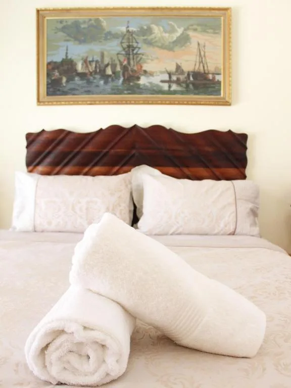 Neatly made bed with rolled white towels and framed maritime artwork