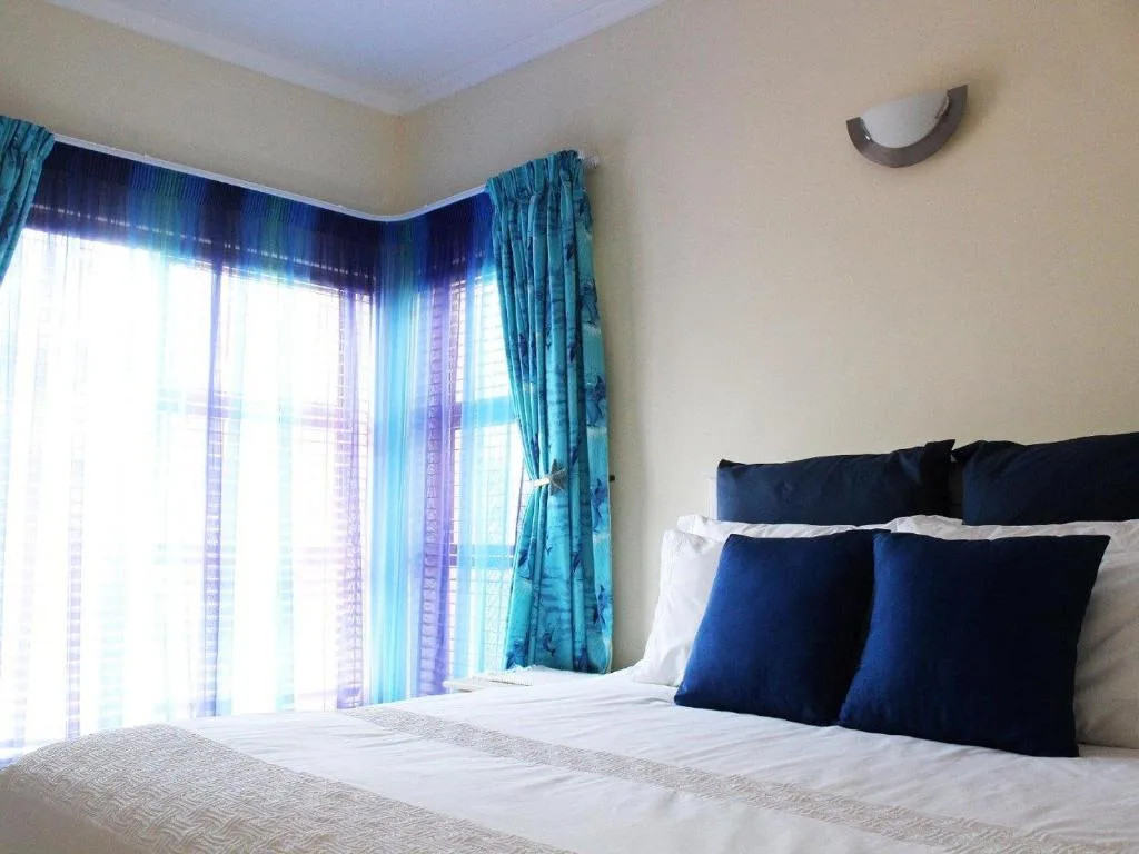 Bright bedroom with double bed, blue pillows, turquoise curtains and windows