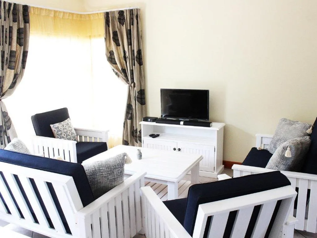 Bright living room with white furniture, TV, and patterned curtains