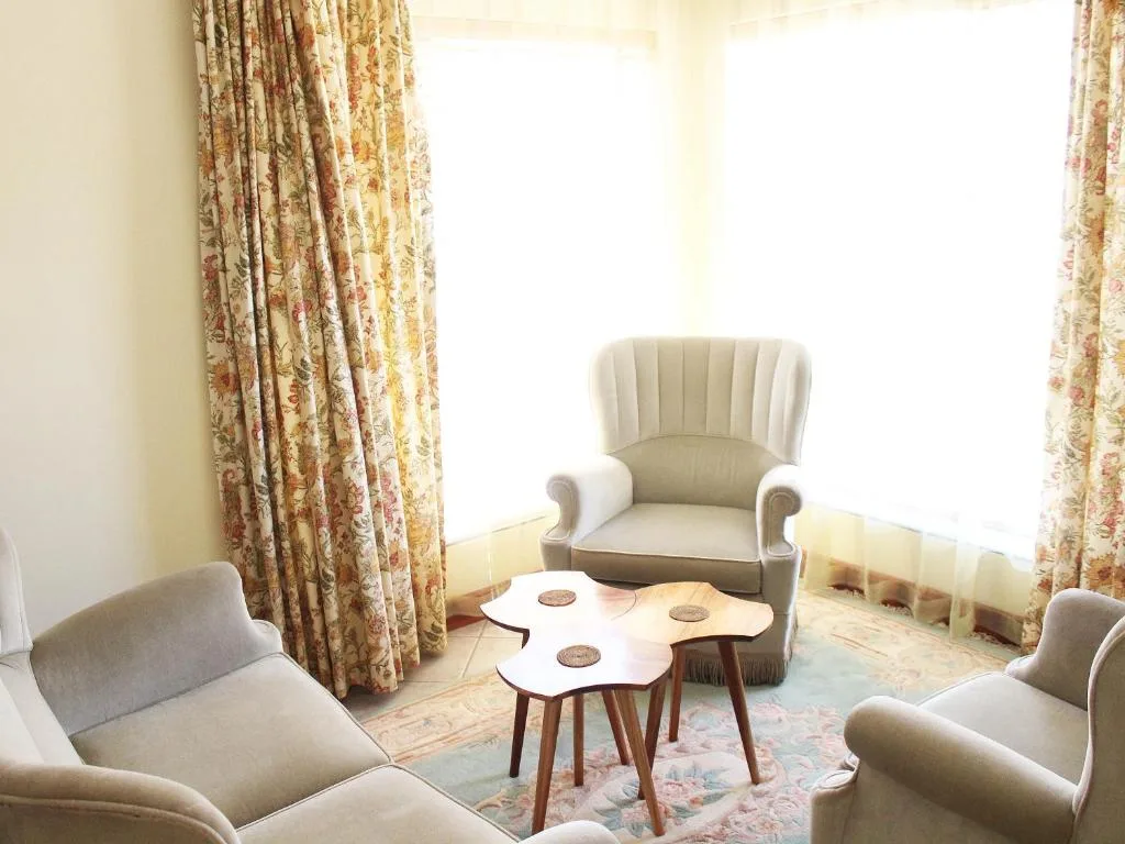 Bright lounge with cream armchairs, wooden side table, and patterned curtains