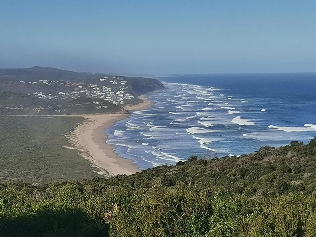 Panoramic coastal view of sandy beach, rolling waves, and hillside settlement
