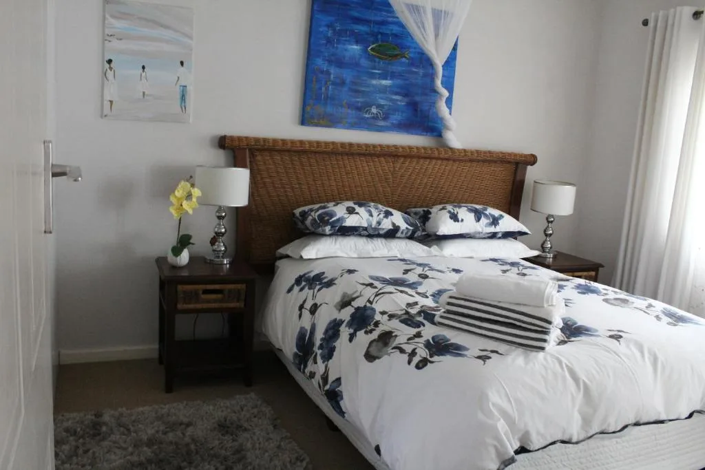 Spacious bedroom with woven headboard, blue floral bedding, and coastal artwork