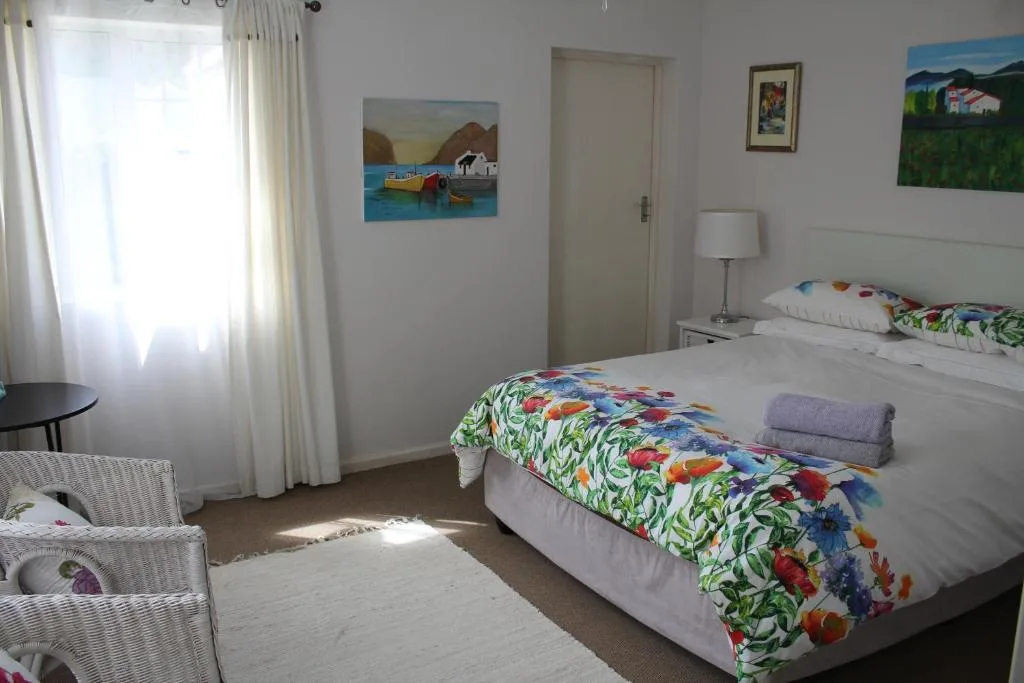 Bright bedroom with two beds, floral bedding, artwork, and large window