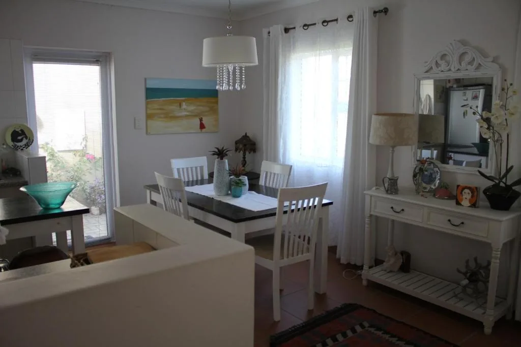 Bright dining room with white chairs and table, pendant lighting, coastal artwork