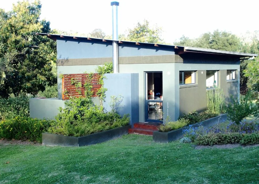 Modern white cottage with dark trim, surrounded by manicured gardens and lawn