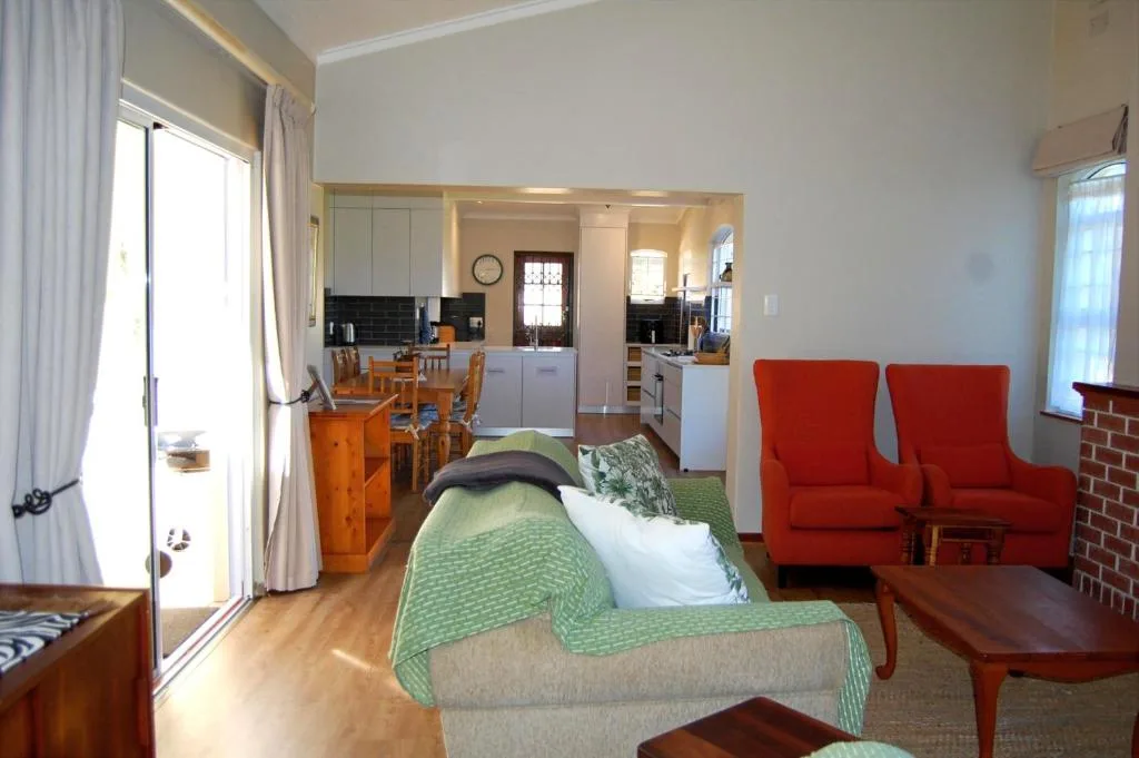 Bright bedroom with green bedspread, red armchairs, and open-plan kitchen view