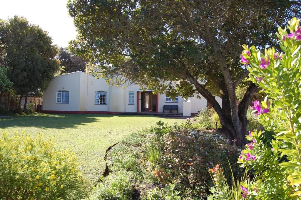 White holiday home surrounded by lush garden and mature trees with flowering shrubs in foreground