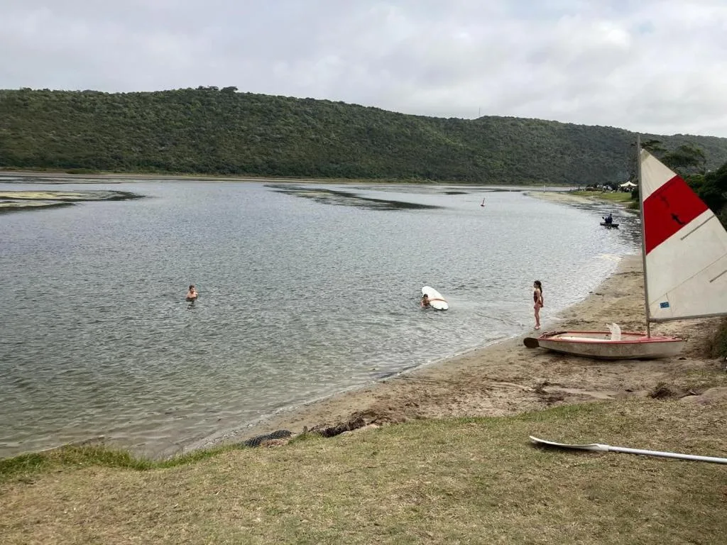 Scenic lagoon view with boats, swimmers, and forested hills beyond