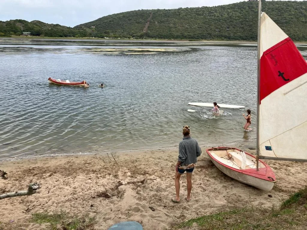 Scenic lagoon view with boats, beach, forested hills, swimmers enjoying water