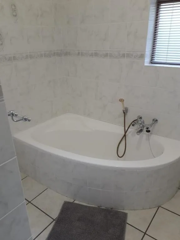 White corner bathtub with chrome fixtures and tiled walls in bathroom