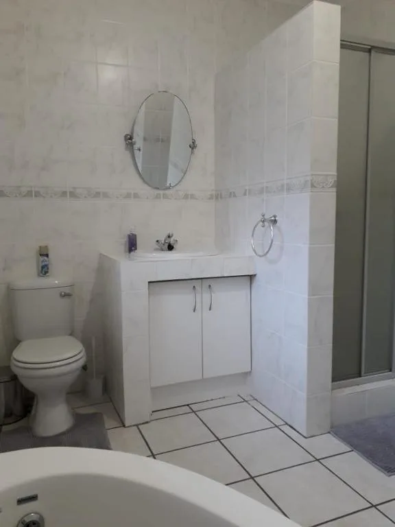 Clean white bathroom with vanity, oval mirror, toilet, and shower enclosure