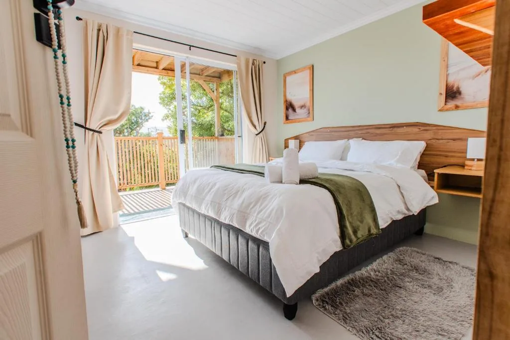 Bright bedroom with double bed, wooden headboard, deck access with green trees