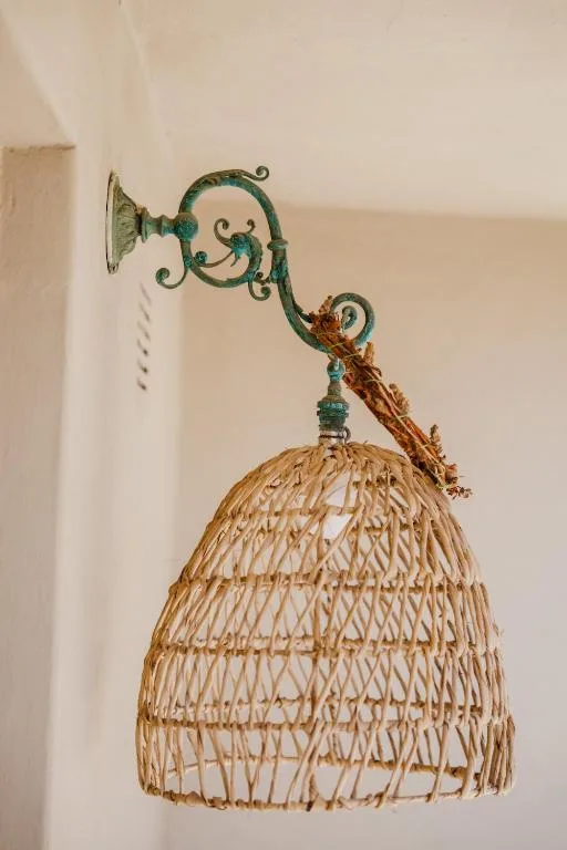 Decorative woven pendant light with ornate green metal bracket on white wall