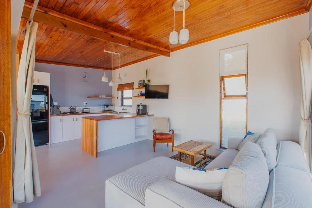 Open-plan lounge with sofa, wooden ceiling beams, and kitchen area visible