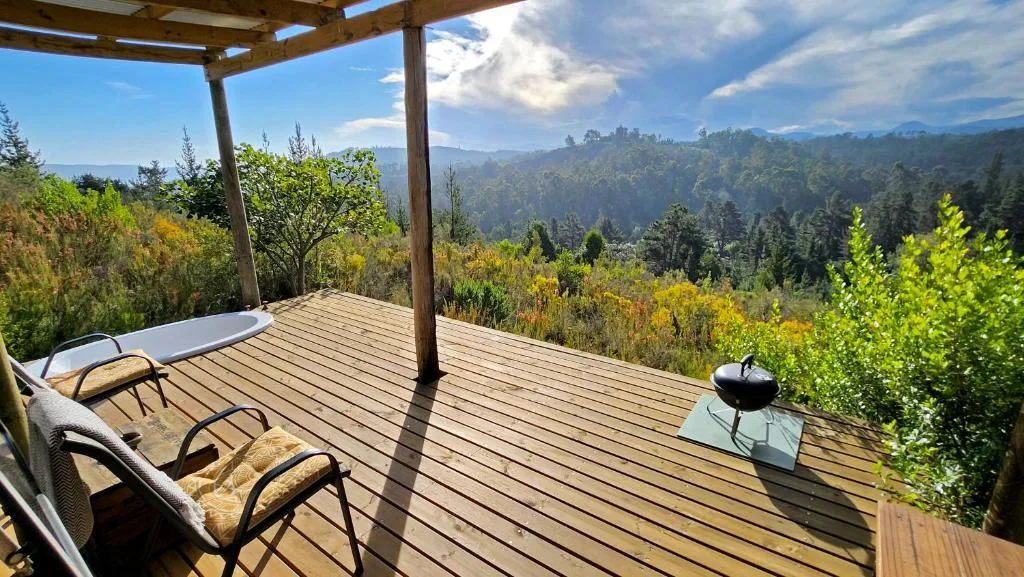Wooden deck with lounge chairs overlooking forested mountain valley landscape