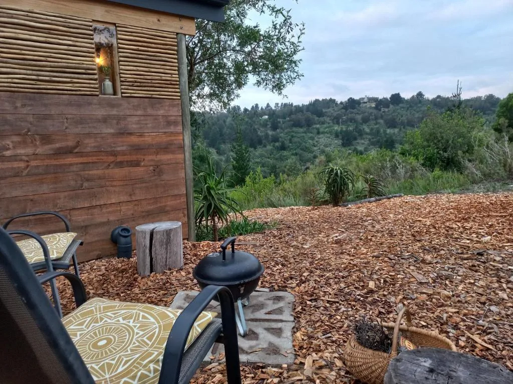 Outdoor seating area with braai, chairs, and forested hillside views