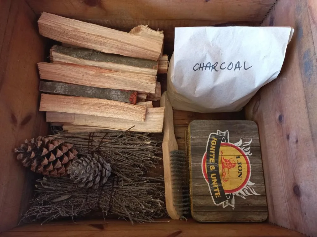 Wooden box containing firewood, charcoal bag, and braai accessories