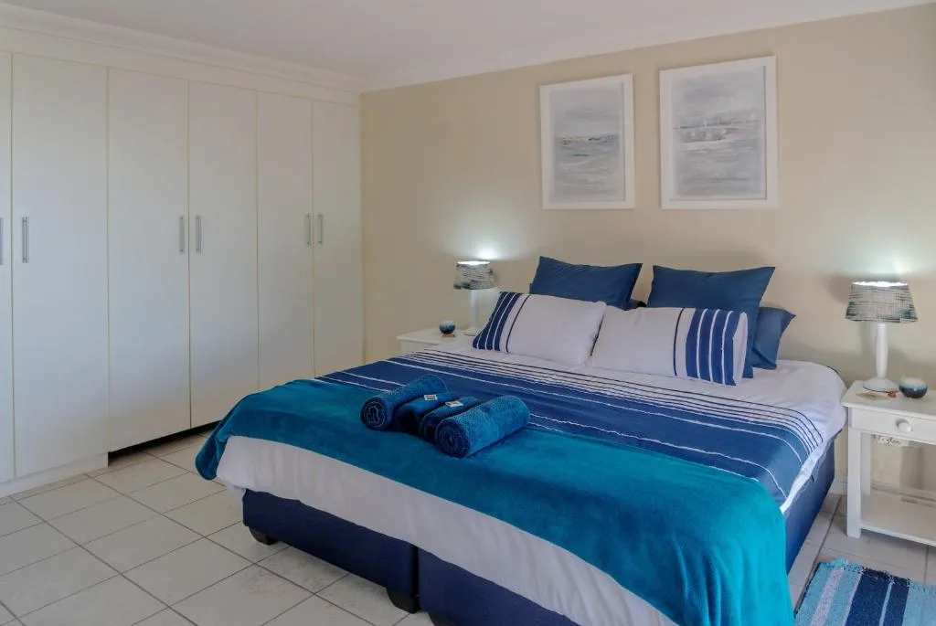 Bright bedroom with blue and white bedding, white wardrobe, and coastal artwork